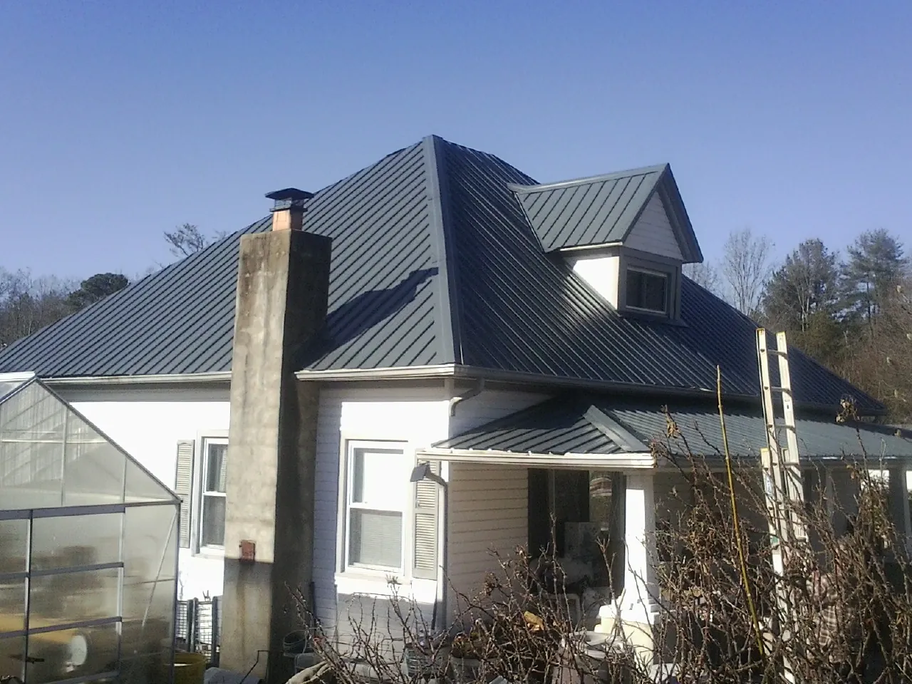Dark blue standing seam metal roof on a white farmhouse with dormer — Slate & Tile Roof Repair by Roofing Brothers in Whitten