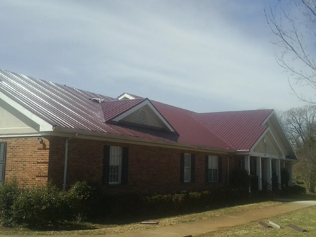 Red metal roof with gabled entries on a long brick building, from a Hail Damage Roof Repair job in Whitten