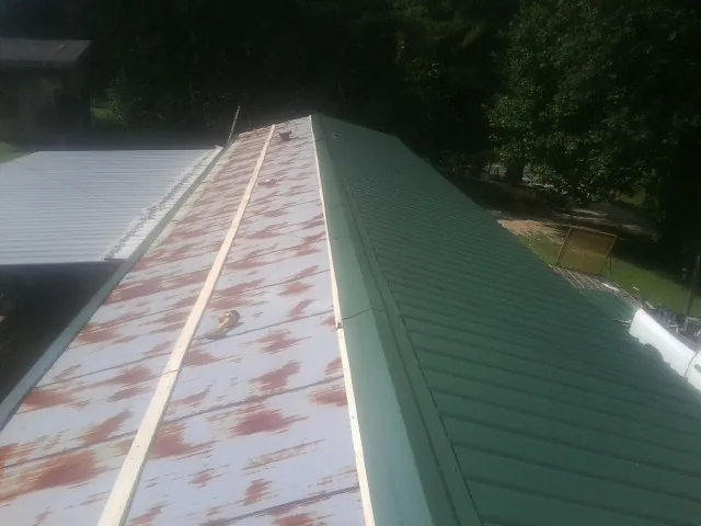 Old rusted panels beside newly installed green metal roofing — Wind Damage Roof Repair by Roofing Brothers in Whitten