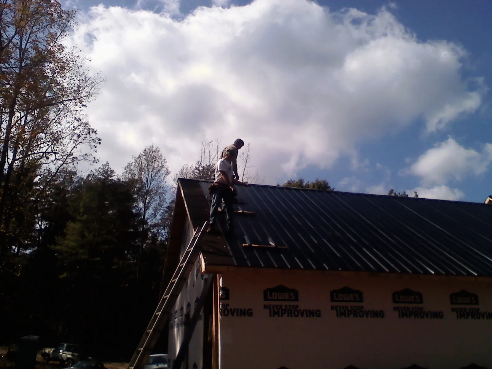 Roofer fastening dark metal panels high against a cloudy sky, from a Roof Inspection job in Whitten