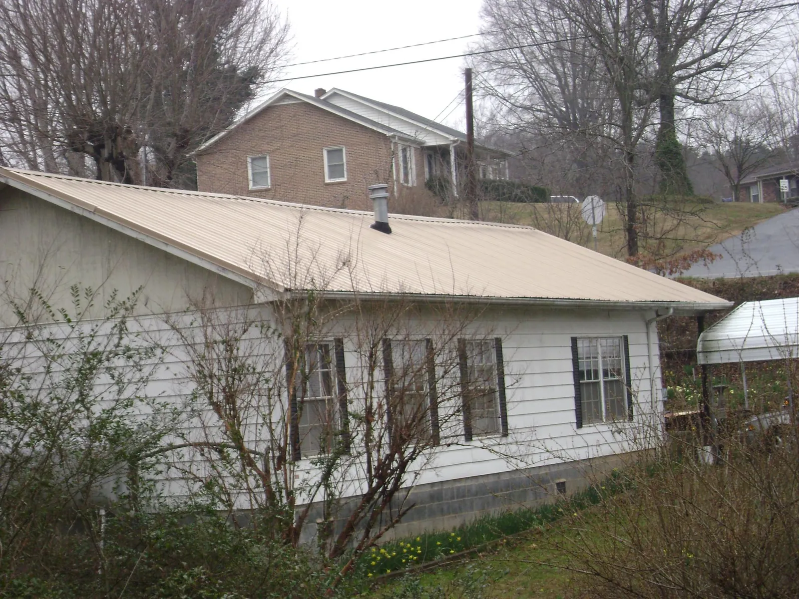 Tan metal roof on a white sided house set into a hillside — Commercial Roofing by Roofing Brothers in Whitten