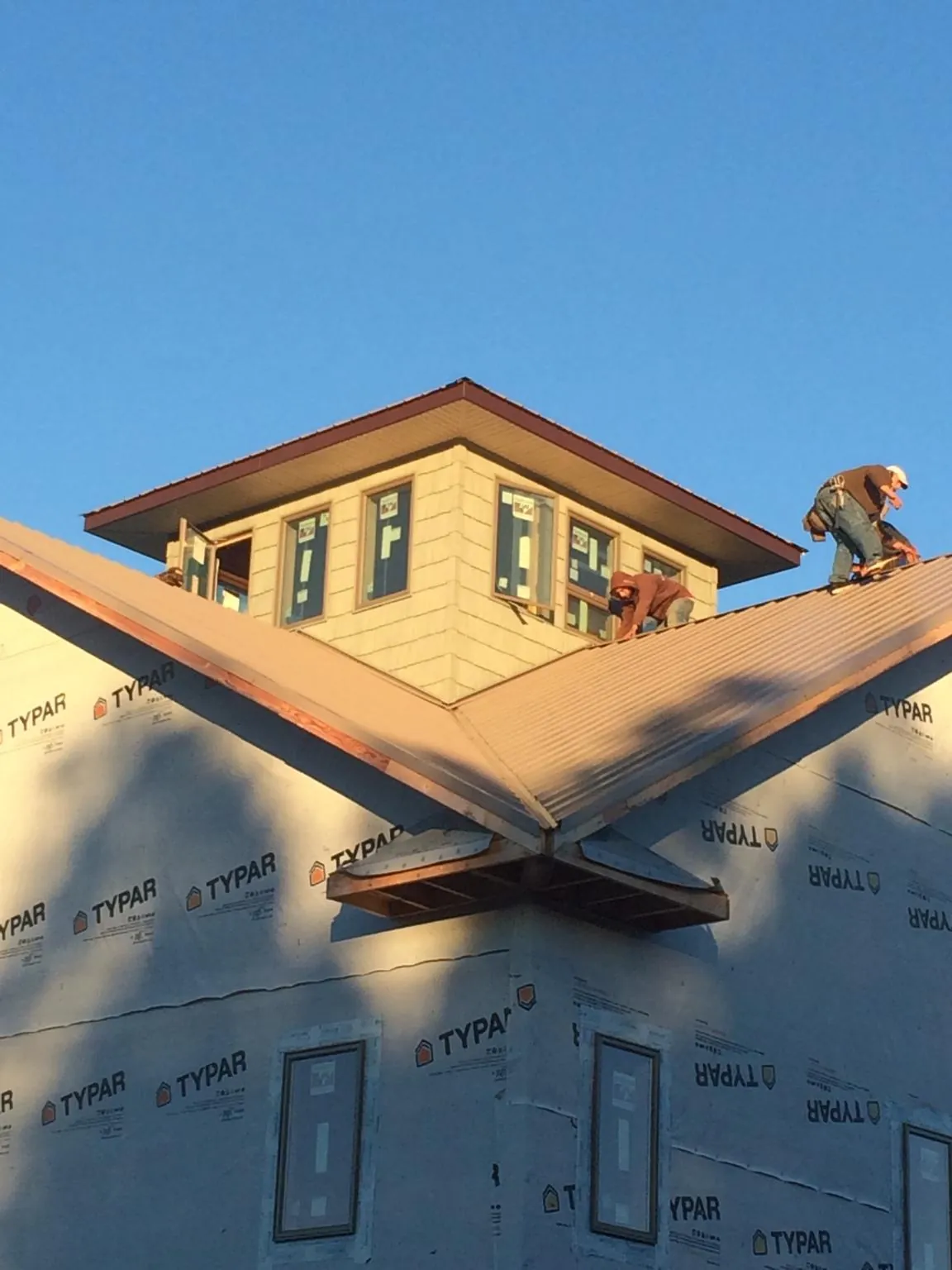 Roofers working around a rooftop cupola on a new metal roof at sunset — Roof Waterproofing in Whitten by Roofing Brothers